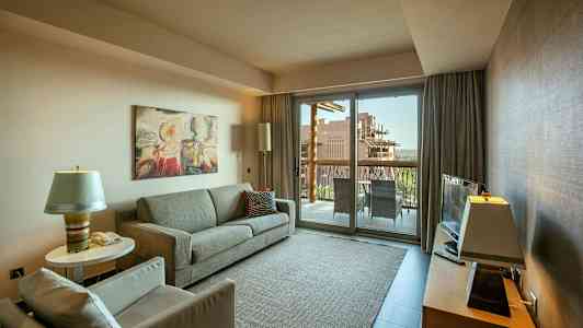 En stue med en sofa, lænestol og et sofabord, et fjernsyn på et møbel samt en glasdør, der fører ud til en altan. (AI-genereret tekst)