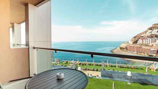 Udsigt fra en altan mod havet og en frodig hotelhave. (AI-genereret tekst)