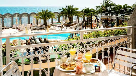 Udsigt fra en balkon med morgenmadsservering mod poolområde og havet. (AI-genereret tekst)