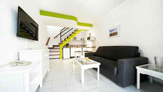 Et hotelværelse med sofa, sofabord, tv og lille køkkenområde. (AI-genereret tekst)