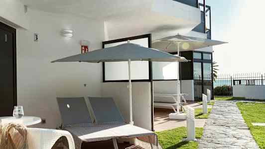 Udendørsområde med to liggestole og parasoller ved en bygning. (AI-genereret tekst)