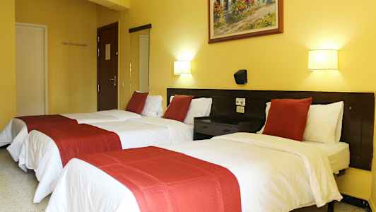 Hotelværelse med to enkeltsenge, hvide lagner og røde dekorative sengetæpper. (AI-genereret tekst)