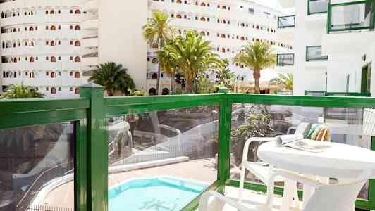 Altan med bord og stole, udsigt over en pool og omkringliggende bygninger. (AI-genereret tekst)