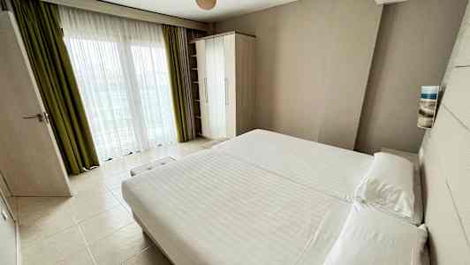 Et hotelværelse med en stor seng, garderobe og vindue med gardiner. (AI-genereret tekst)