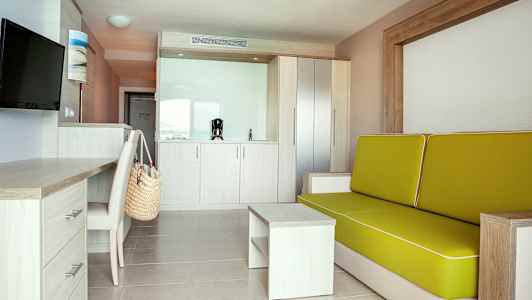 Moderne hotelværelse med sofa, skrivebord og tekøkken. (AI-genereret tekst)