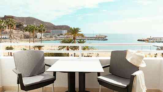 To stole og et bord på en altan med udsigt over en strand og havet. (AI-genereret tekst)