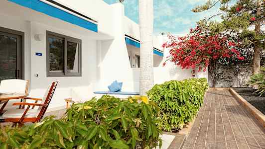 Terrasse med siddepladser foran en hvid bygning med blå detaljer. (AI-genereret tekst)