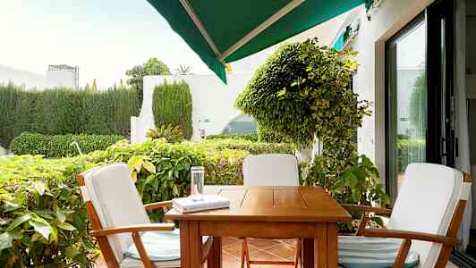 Havemøbler med tre stole omkring et bord på en terrasse, omgivet af grønne planter. (AI-genereret tekst)