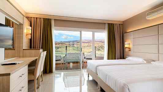 Hotelværelse med to enkeltsenge, skrivebord og udsigt til landskab gennem en glasdør. (AI-genereret tekst)