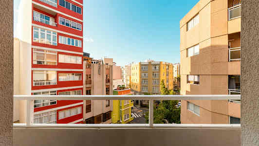 Udsigt fra en altan med flere bygninger og en blå himmel i baggrunden. (AI-genereret tekst)