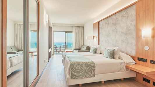 Hotelværelse med dobbeltseng, siddeområde og balkon med havudsigt. (AI-genereret tekst)