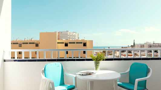 En altan med to stole, et bord og udsigt over bygninger og havet. (AI-genereret tekst)