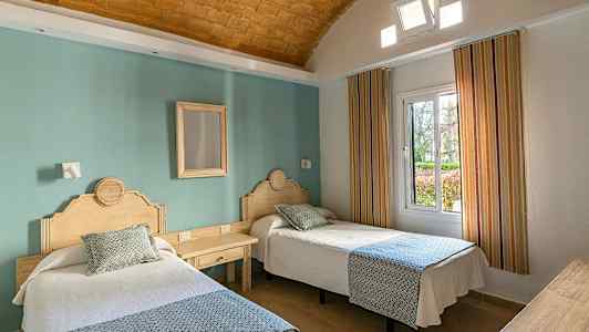 To enkeltsenge med træhovedgavle i et hotelværelse med en grøn væg og vindue. (AI-genereret tekst)