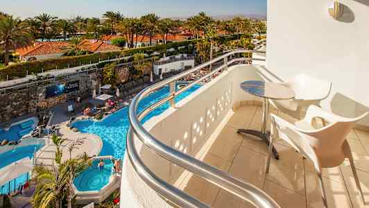 Udsigt fra en balkon med bord og stole mod en pool og palmer. (AI-genereret tekst)