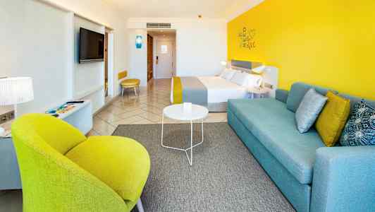 Moderne indrettet hotelværelse med farverige detaljer som gul stol og blå sofa. (AI-genereret tekst)