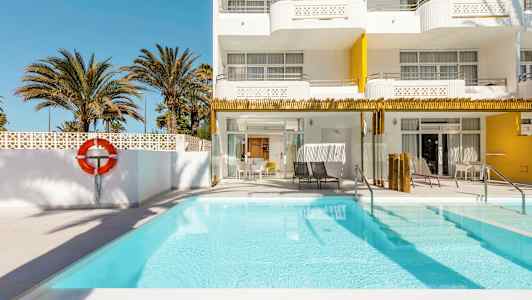 Udendørs pool ved et hotel med hvide og gule facader, omgivet af palmer. (AI-genereret tekst)