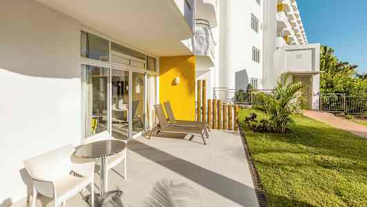 En solrig terrasse med to stole og et bord ved siden af glasdøre. (AI-genereret tekst)