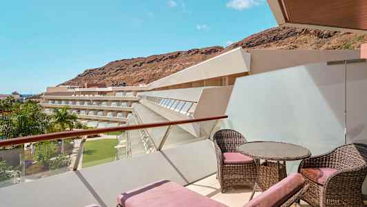 En terrasse med liggestole og møbler med udsigt over hotelbygninger, palmetræer og bjerge. (AI-genereret tekst)