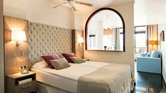 Dobbeltværelse med bred seng, lamper og dekorative puder. (AI-genereret tekst)