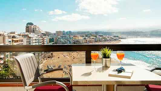 En balkon med bord og stole, udsigt over en strand og by. (AI-genereret tekst)