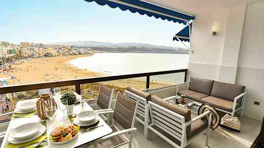 Et møbleret altanområde med udsigt over en strand og havet. (AI-genereret tekst)