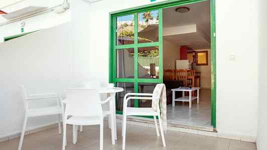 Terrasse med hvide møbler foran en grøn dørramme, der fører ind til en lejlighed. (AI-genereret tekst)