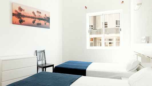 To enkeltsenge i et lyst værelse med et blåt tæppe på hver seng. (AI-genereret tekst)