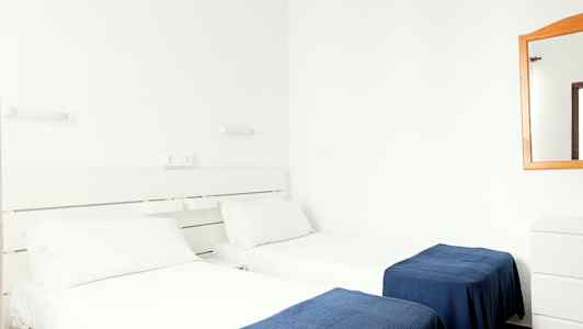 To enkeltsenge med hvide lagner og blå tæpper i et hotelværelse. (AI-genereret tekst)