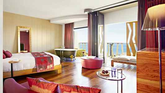 Et hotelværelse med en seng, badekar, siddeområde og udsigt over havet. (AI-genereret tekst)