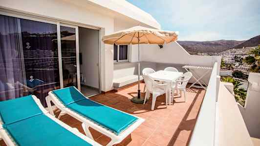 En terrasse med to solsenge, havemøbler med parasol og udsigt over en by og bjerge i det fjerne. (AI-genereret tekst)