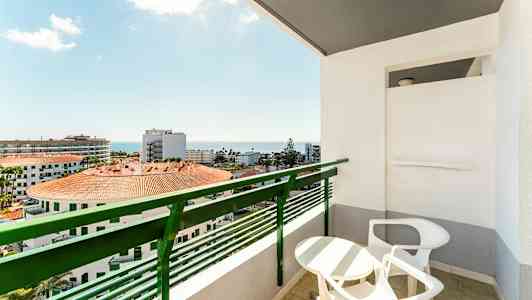 Altan med bord og stole samt udsigt over bygninger og havet. (AI-genereret tekst)