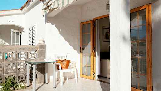 Terrasse med hvid bygning, bord og stol, samt en dør, der fører ind i huset. (AI-genereret tekst)