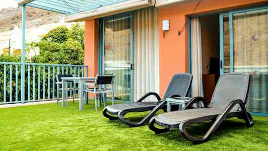 En terrasse med liggestole og et bord med stole, samt grøn kunstig græsplæne. (AI-genereret tekst)