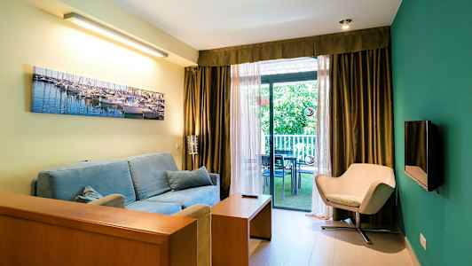 Stue med blå sofa, beige stol og store vinduer ud mod en altan. (AI-genereret tekst)