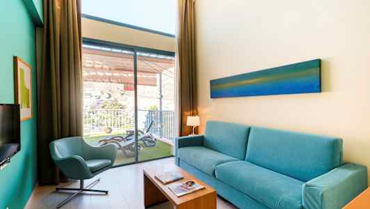 Stue med blå sofa, stol og udsigt til en altan. (AI-genereret tekst)