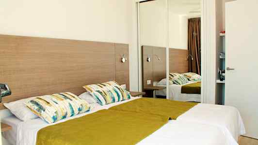 Dobbeltværelse med to enkeltsenge, et spejl og træmøbler. (AI-genereret tekst)