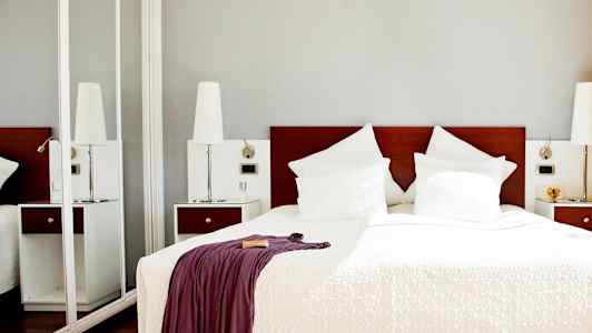 Et hotelværelse med en dobbeltseng med hvidt sengetøj og puder samt et tæppe med et draperet tæppe. (AI-genereret tekst)