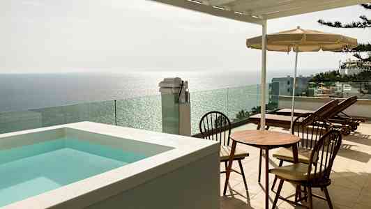 Terrasse med en lille pool, bord og stole samt liggestole med udsigt over havet. (AI-genereret tekst)