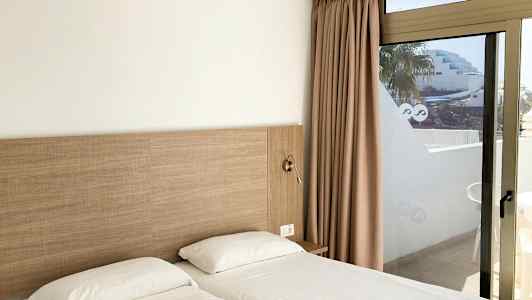 To enkeltsenge med hvidt sengetøj ved siden af en glasdør med udsigt. (AI-genereret tekst)