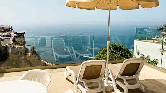 To liggestole med en parasol på en terrasse med havudsigt. (AI-genereret tekst)