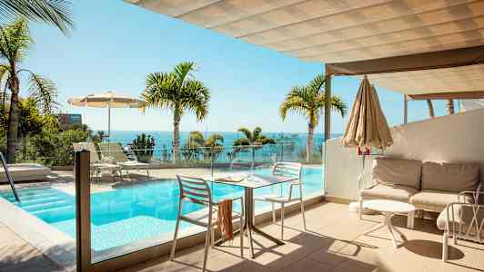 En terrasse med en pool og udsigt over havet, omgivet af palmer. (AI-genereret tekst)