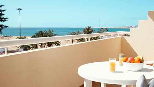 Altan med havudsigt, et bord med frugtskål og glas med juice. (AI-genereret tekst)