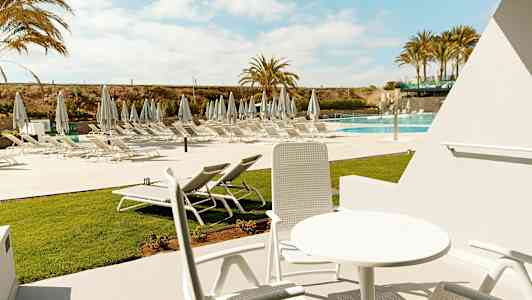 Udendørsmøbler i solrig omgivelser med udsigt over liggestole ved poolen. (AI-genereret tekst)