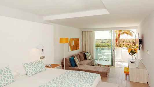 Et moderne hotelværelse med seng, sofa, dekorativt træbord og altan med udsigt. (AI-genereret tekst)