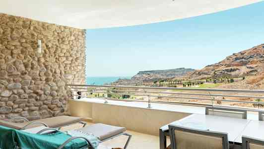 Terrasse med liggestole og udsigt over havet og et bjerglandskab. (AI-genereret tekst)