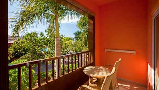 Altan med to flettede stole og bord, omgivet af planter og palmer. (AI-genereret tekst)