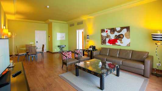 Stue med grøn væg, brun sofa, kunst på væggen og et spisebord med stole. (AI-genereret tekst)