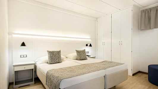 Dobbeltværelse med hvide vægge, dobbeltseng, sengelamper og garderobe. (AI-genereret tekst)