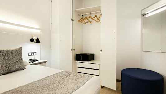 Et hotelværelse med åben garderobe, seng og spejl. (AI-genereret tekst)