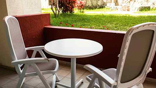 To siddepladser med bord på en altan med udsigt til græsplæne og stenmur. (AI-genereret tekst)